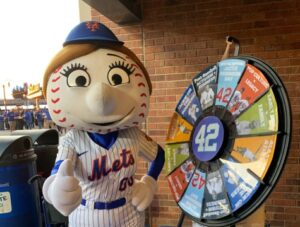 Mrs. Met mascot gives a thumbs up at the Jackie Robinson Museum table next to the trivia game wheel.